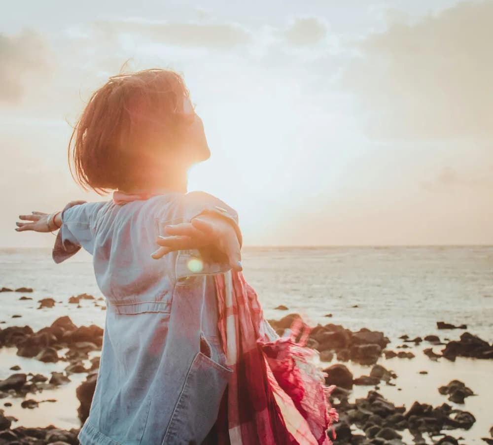 A woman with her arms open at the ocean at sunrise