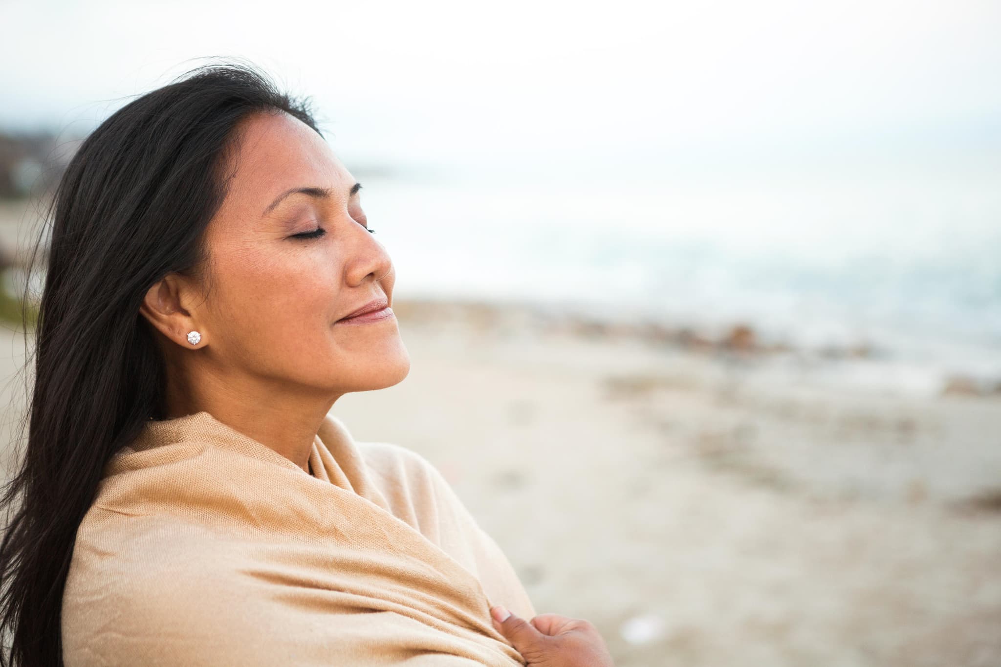 A woman with her eyes closed, breathing calmly by the sea